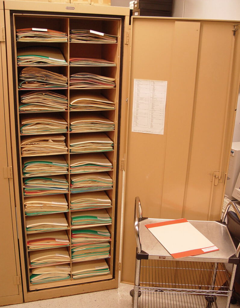 Herbarium cabinet, showing folders of dried plant specimens, color-coded by region.
